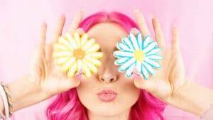 Fille aux cheveux roses avec des gateaux en forme de fleur devant les yeux