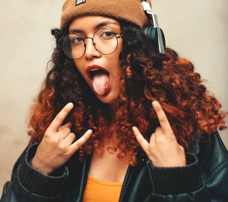 jeune femme aux cheveux bouclés tirant la langue et faisant des signes rock n' roll avec ses mains