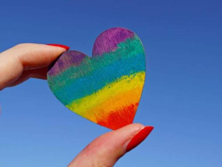Petit coeur couleur arc-en-ciel tenu dans la main d'une femme